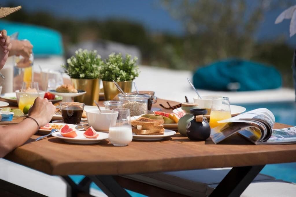 Une table en bois avec des aliments pour le petit-déjeuner, un magazine et une vue sur la piscine.