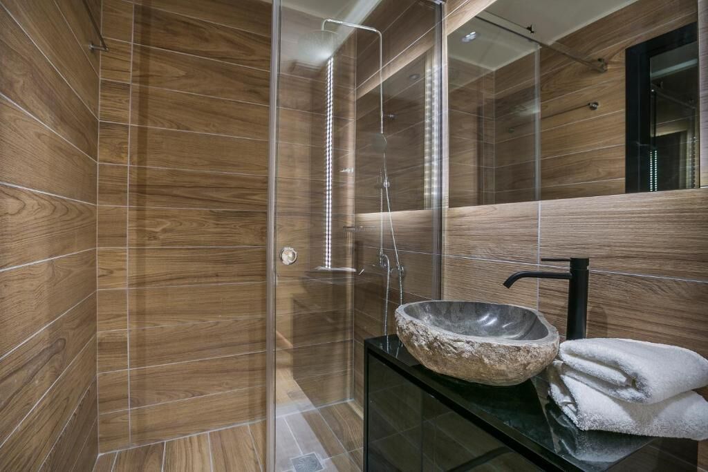 Une salle de bain moderne avec des murs en bois, une douche en verre, un lavabo en pierre et un robinet noir.