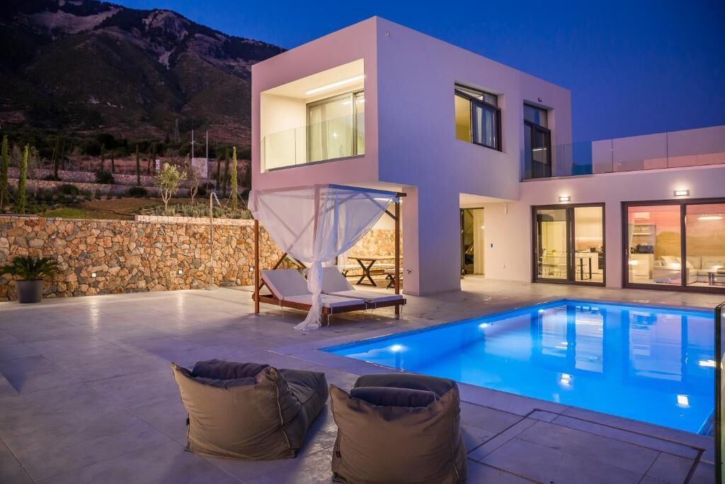 A modern two-story house with a swimming pool, stone wall, and outdoor seating.