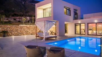 A modern two-story house with a swimming pool, stone wall, and outdoor seating.