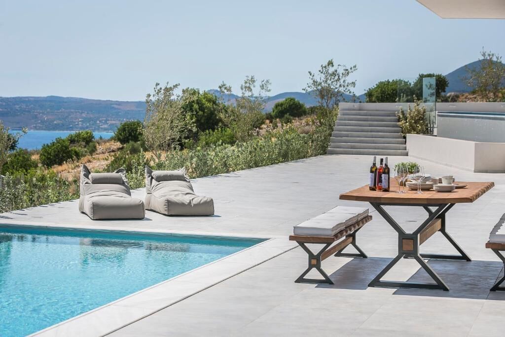 A poolside area with a table set for dining, outdoor seating, and a view of the landscape.