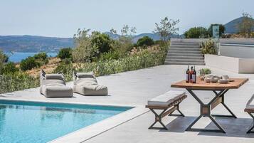 A poolside area with a table set for dining, outdoor seating, and a view of the landscape.