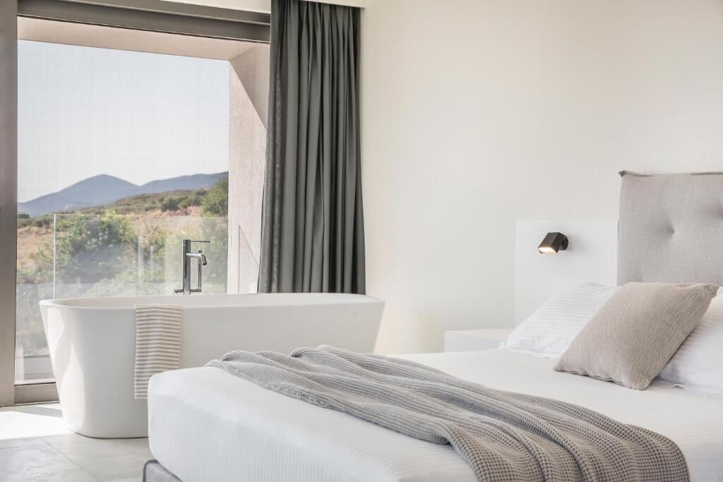 A modern bedroom with a large window, a bathtub, and a bed with a headboard.