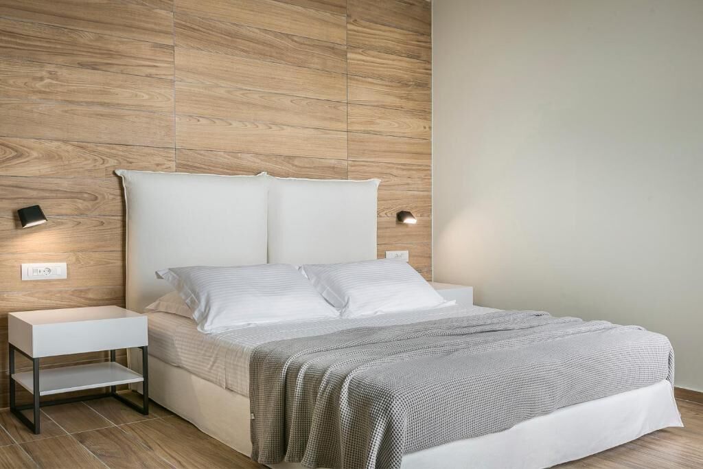 A modern bedroom with a wooden headboard, a white bedside table, and a bed with a grey patterned bedspread.