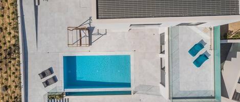 A modern pool area with a rectangular pool, lounge chairs, and a glass-enclosed section.