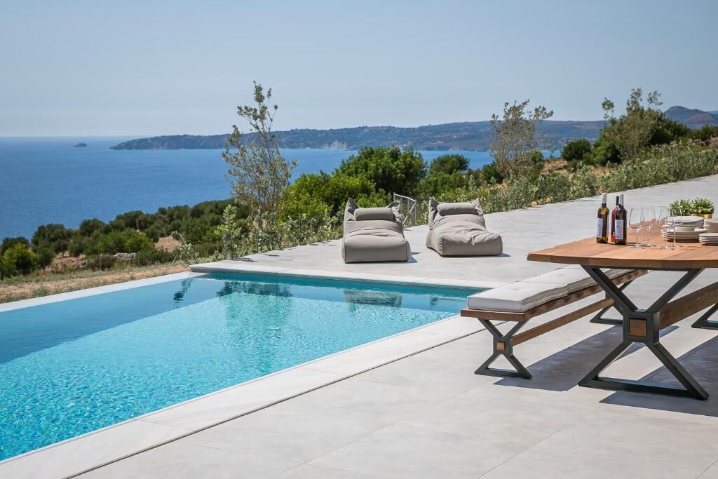 Une piscine bordée de chaises longues et dotée d’une table, offrant une vue sur un paysage côtier.