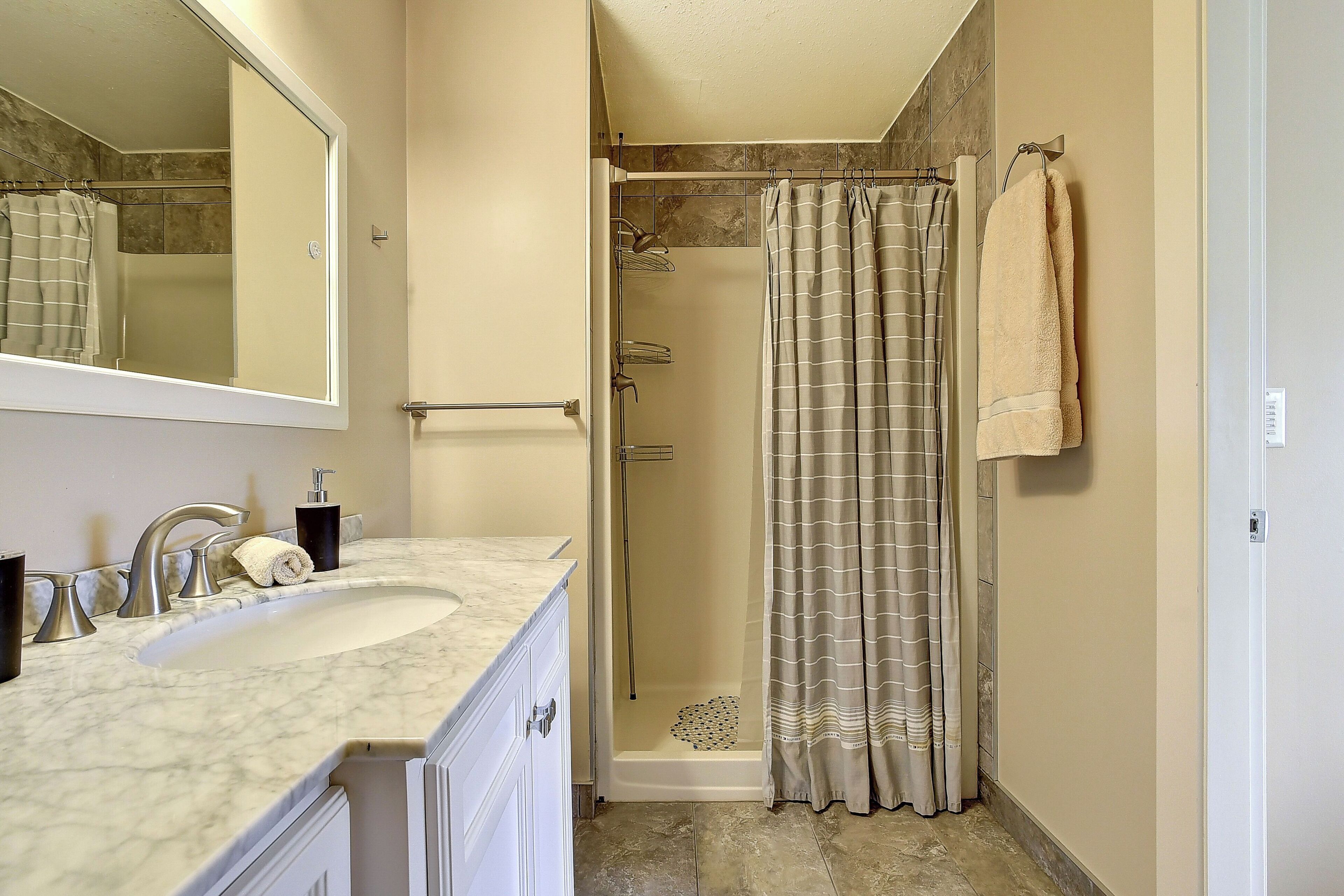 A bathroom with a sink, mirror, shower, and towel rack.