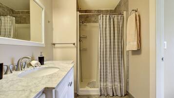 A bathroom with a sink, mirror, shower, and towel rack.