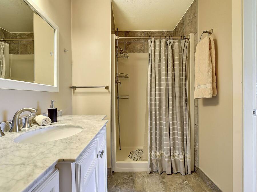 A bathroom with a sink, mirror, shower, and towel rack.