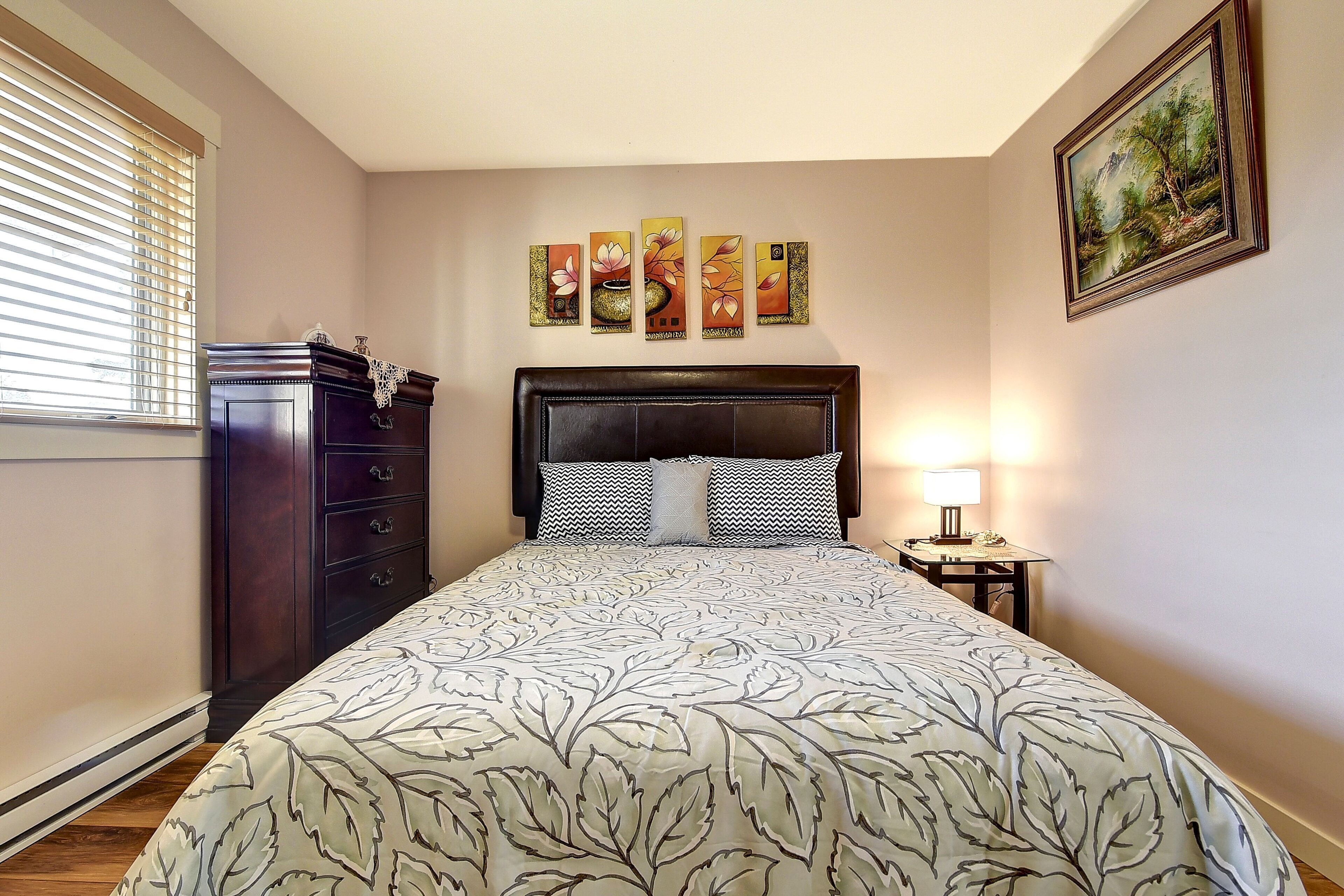 Un dormitorio con una cama grande, un tocador, una mesita de noche con lámpara y una obra de arte en la pared.