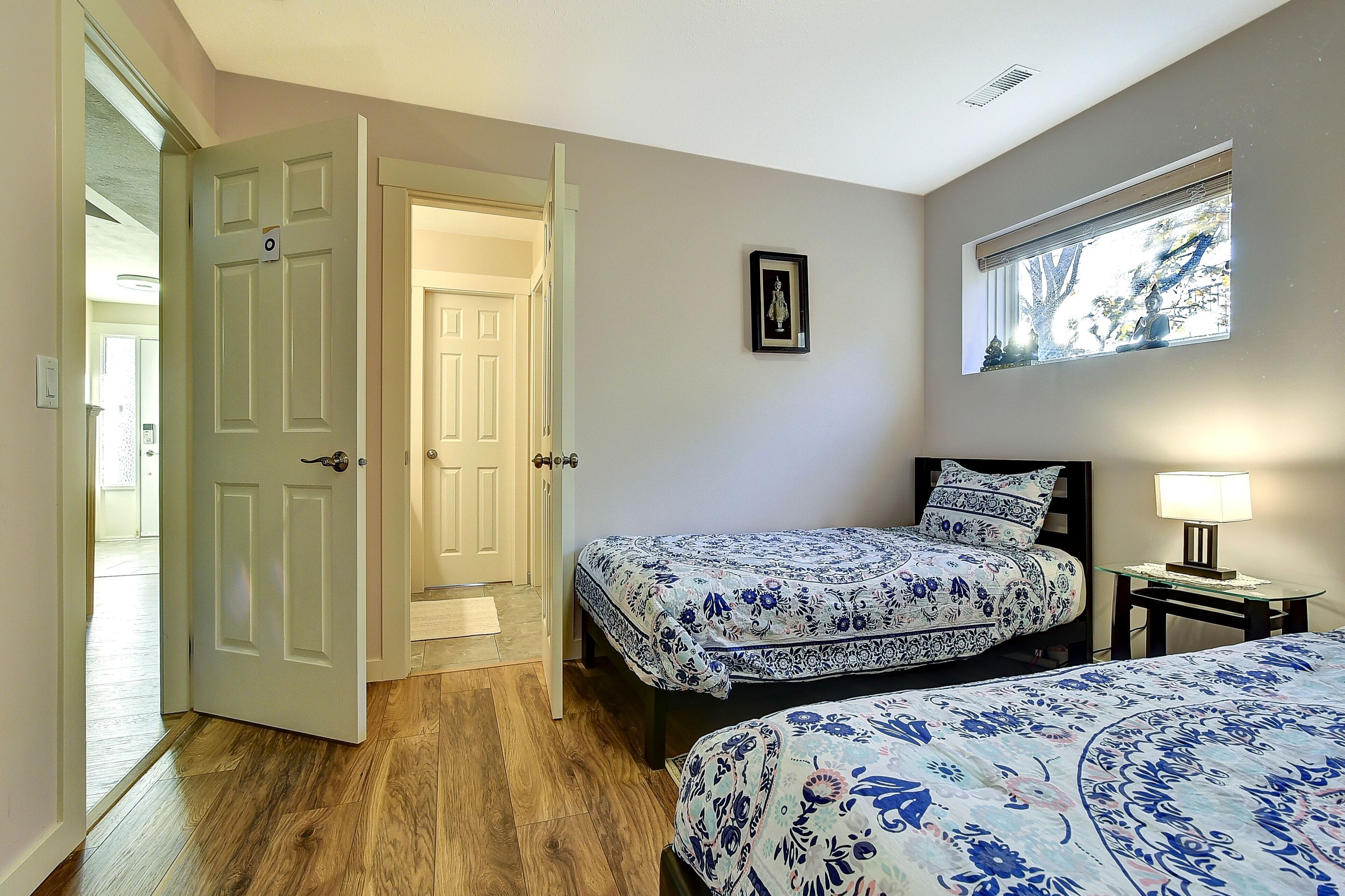 Une chambre avec deux lits, une table de chevet, une fenêtre donnant sur un beau paysage et une porte menant à une autre pièce.