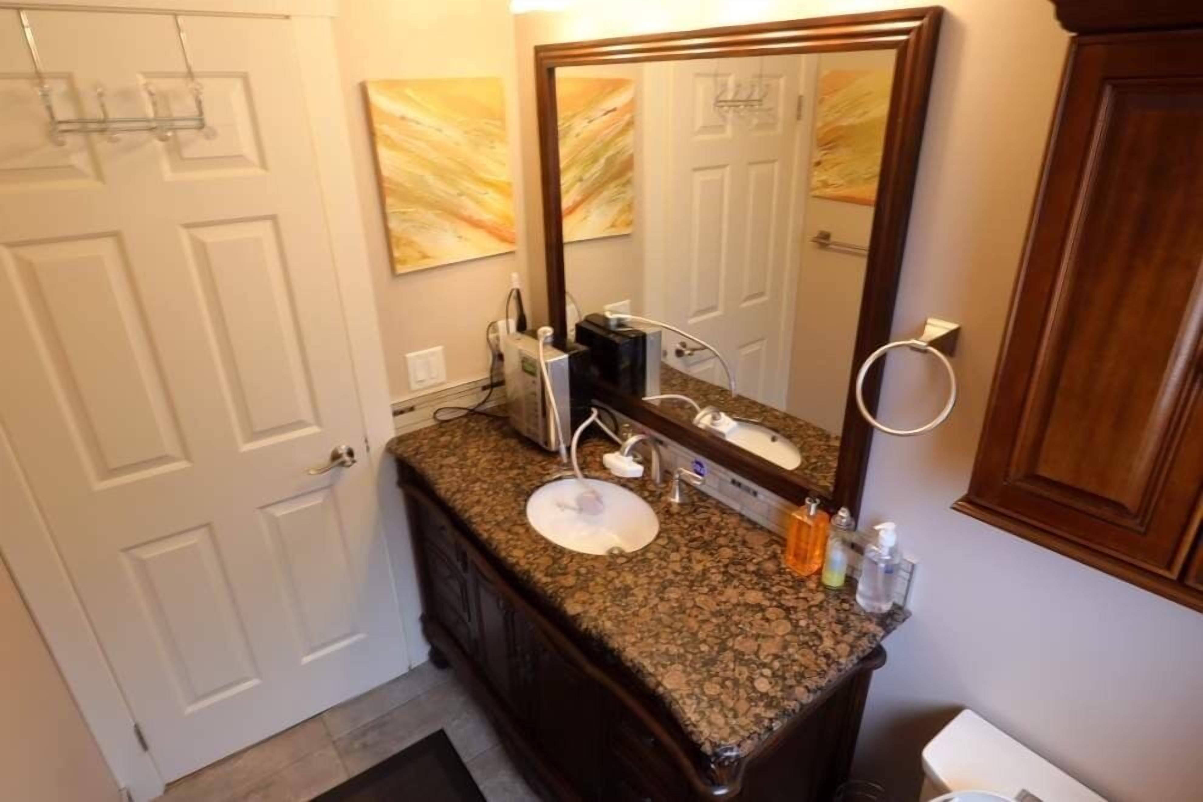 Une salle de bain avec un comptoir en granit, un lavabo blanc, un grand miroir et un meuble en bois.