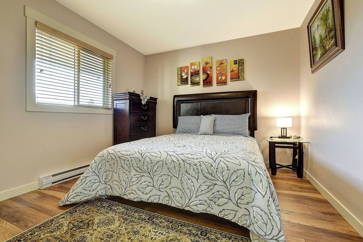 Une chambre à coucher comprenant un lit, une table de chevet, une commode et une fenêtre avec des stores.