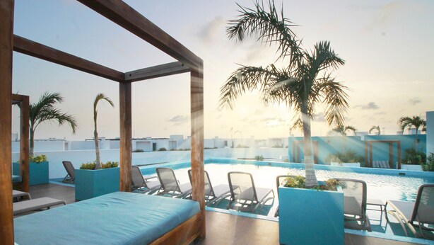 A hotel room with a bed, a pool area with lounge chairs, and palm trees. - The Gallery Apartments (Playa del Carmen)
