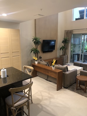 Relax in the spacious living room with a sofa, bench, and flat-screen TV, surrounded by a dining table and potted plants.