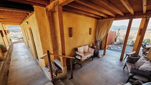Un intérieur en bois avec un canapé et un banc rembourré, un escalier et une vue sur le paysage désertique.