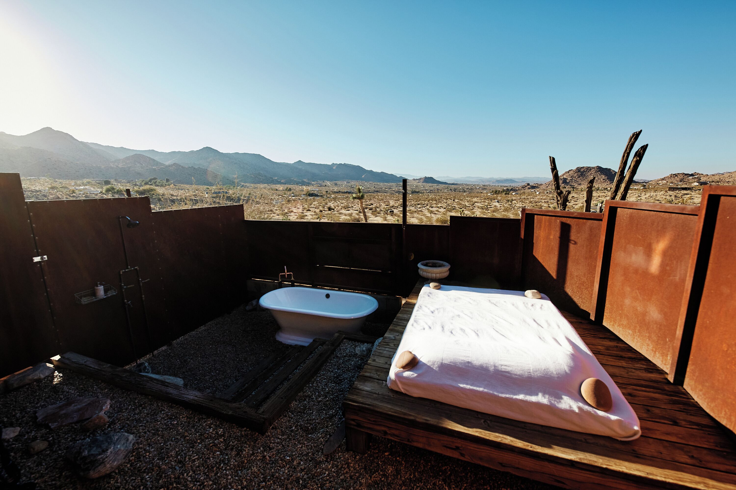 A rustic outdoor bathroom with a bathtub, a wooden bench, and a view of mountains.