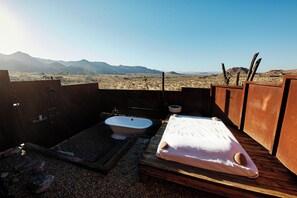 A rustic outdoor bathroom with a bathtub, a wooden bench, and a view of mountains.