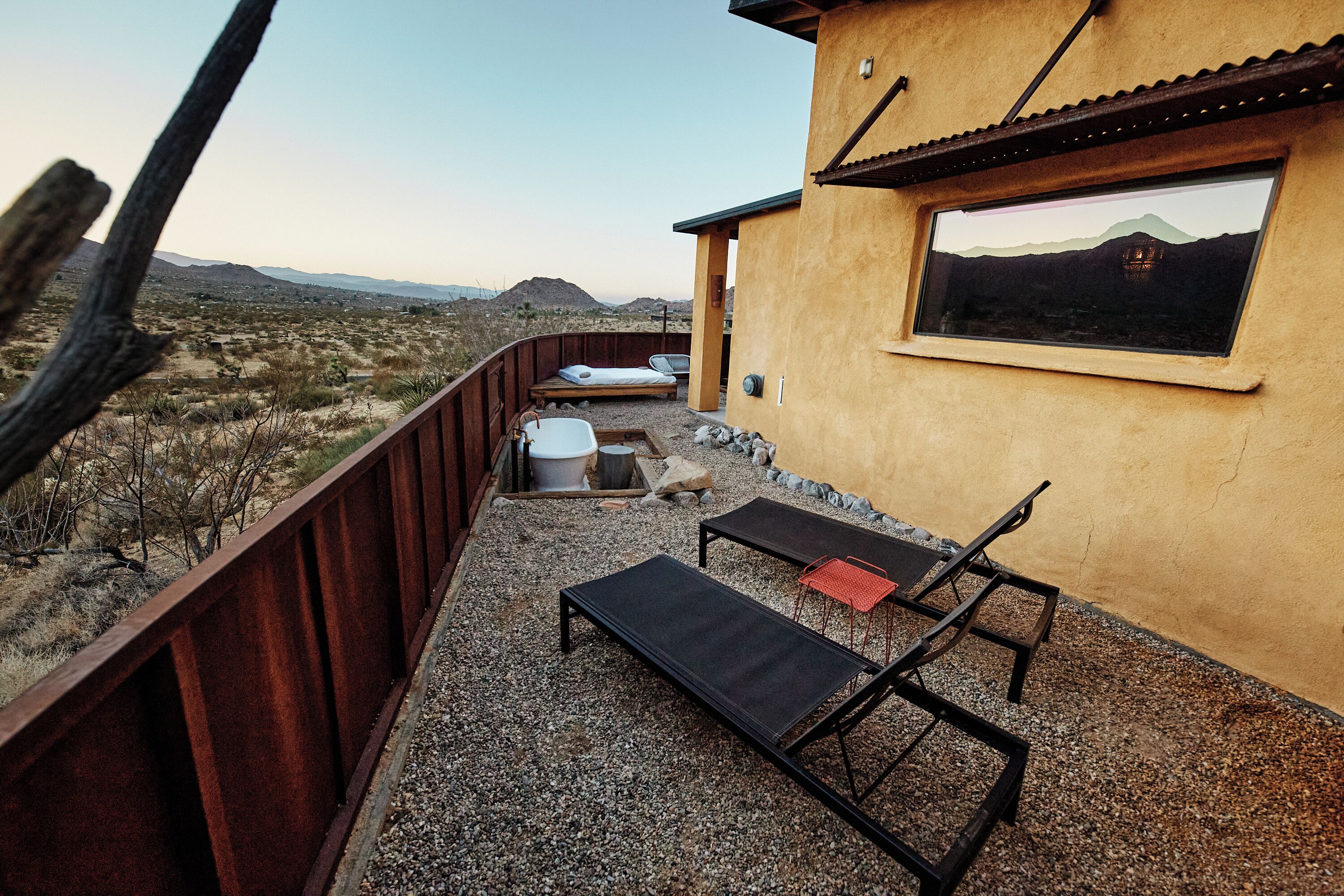 A patio with a metal table and chairs, a small seating area, and a window overlooking a desert landscape.