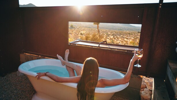 Une personne se détend dans une baignoire, avec vue sur un paysage désertique par la fenêtre.