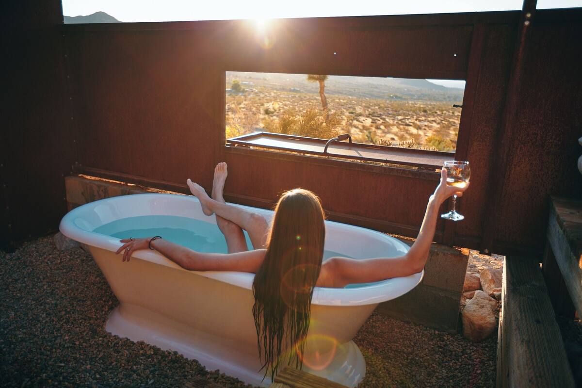 Une personne se détend dans une baignoire, avec vue sur un paysage désertique par la fenêtre.