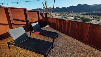 Una terraza en la azotea con dos sillones de descanso, una mesita y vista a un paisaje desértico con montañas al fondo.