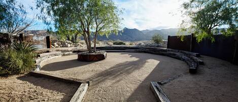 A curved pathway with a wooden bench, surrounded by desert vegetation and a mountainous backdrop.