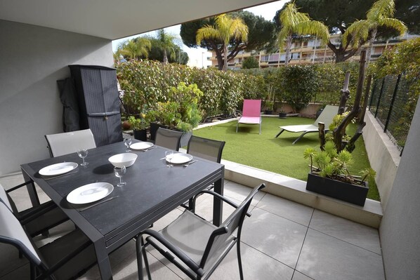 A dining area with a table set for four, outdoor seating, and a view of a well-maintained garden and residential buildings.