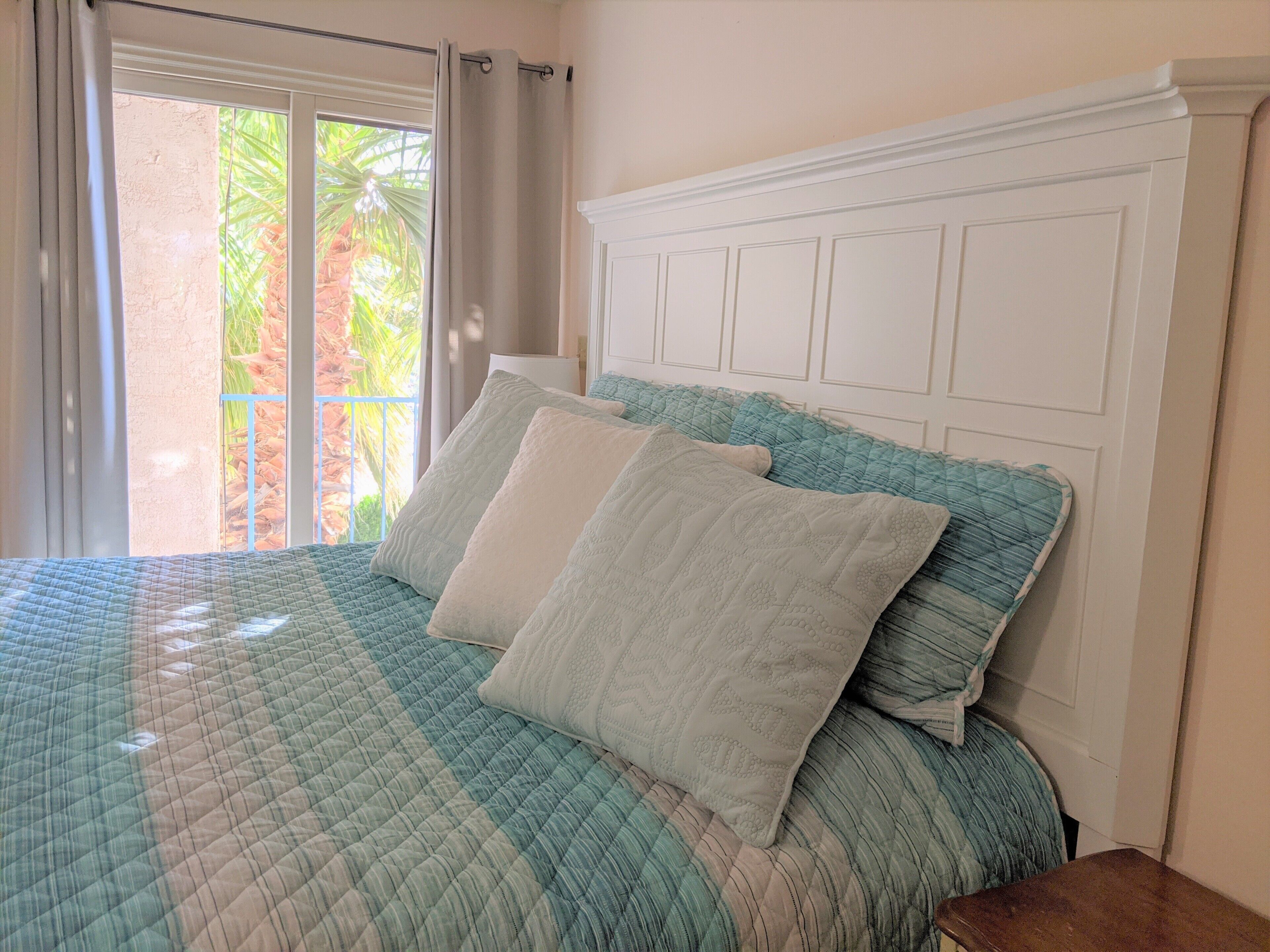 A bed with a quilted blue and white pattern, two pillows, and a white headboard.