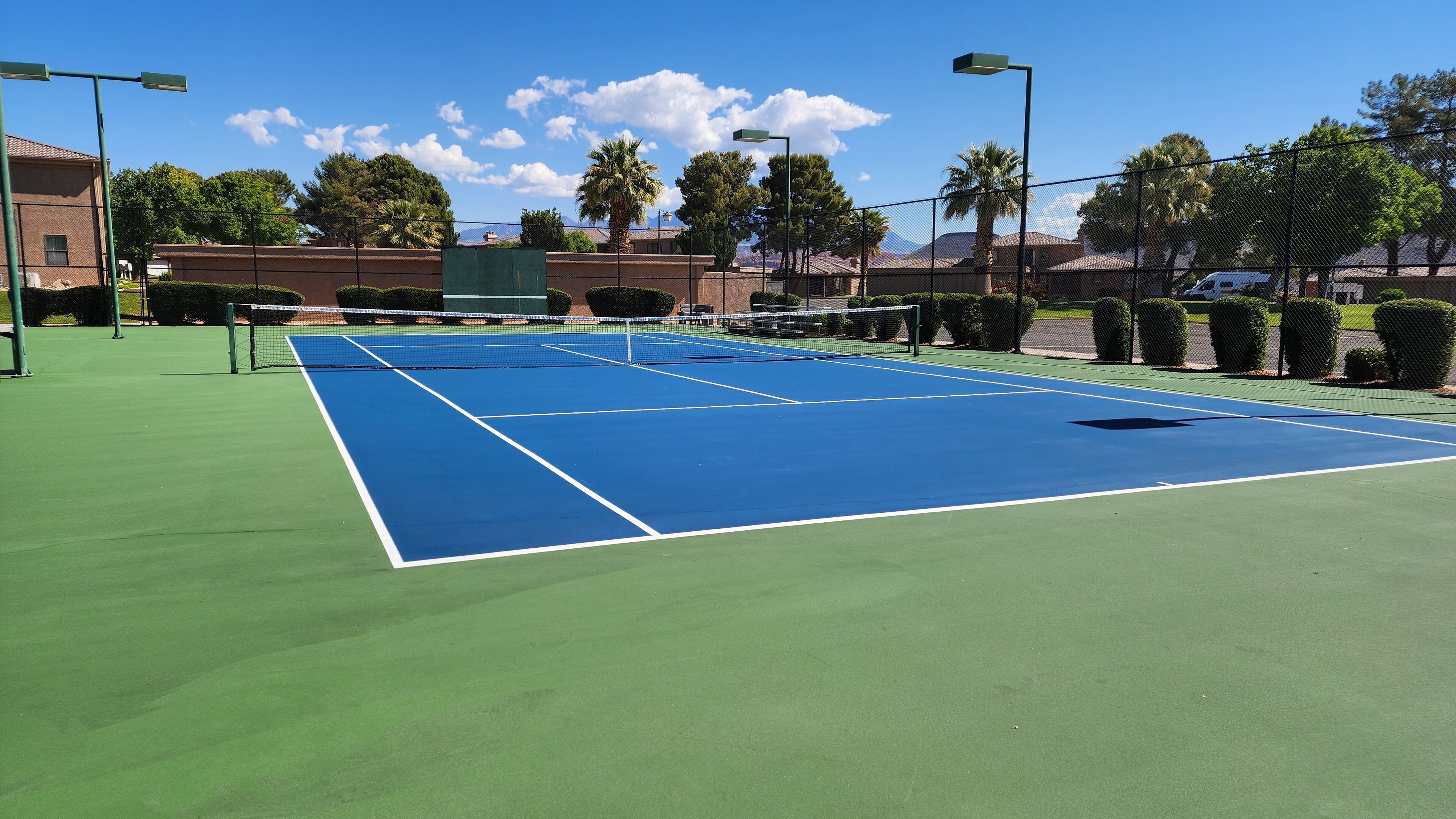 Una cancha de tenis con red, rodeada por una valla y árboles al fondo.