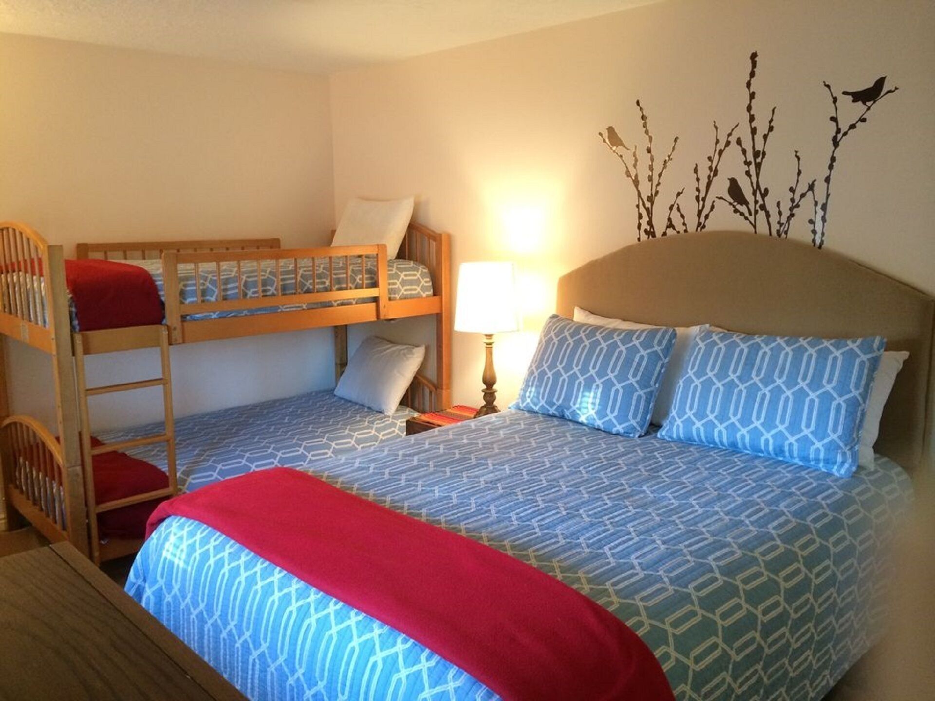Habitación con literas, una colcha estampada, una manta roja y una decoración de ramas con pájaros.