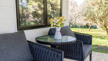 A round glass table with a white vase containing yellow and white flowers, surrounded by dark grey upholstered chairs.
