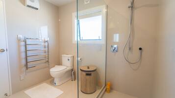 A modern bathroom with a glass shower enclosure, a toilet, a glass-walled vanity, and a towel rack.