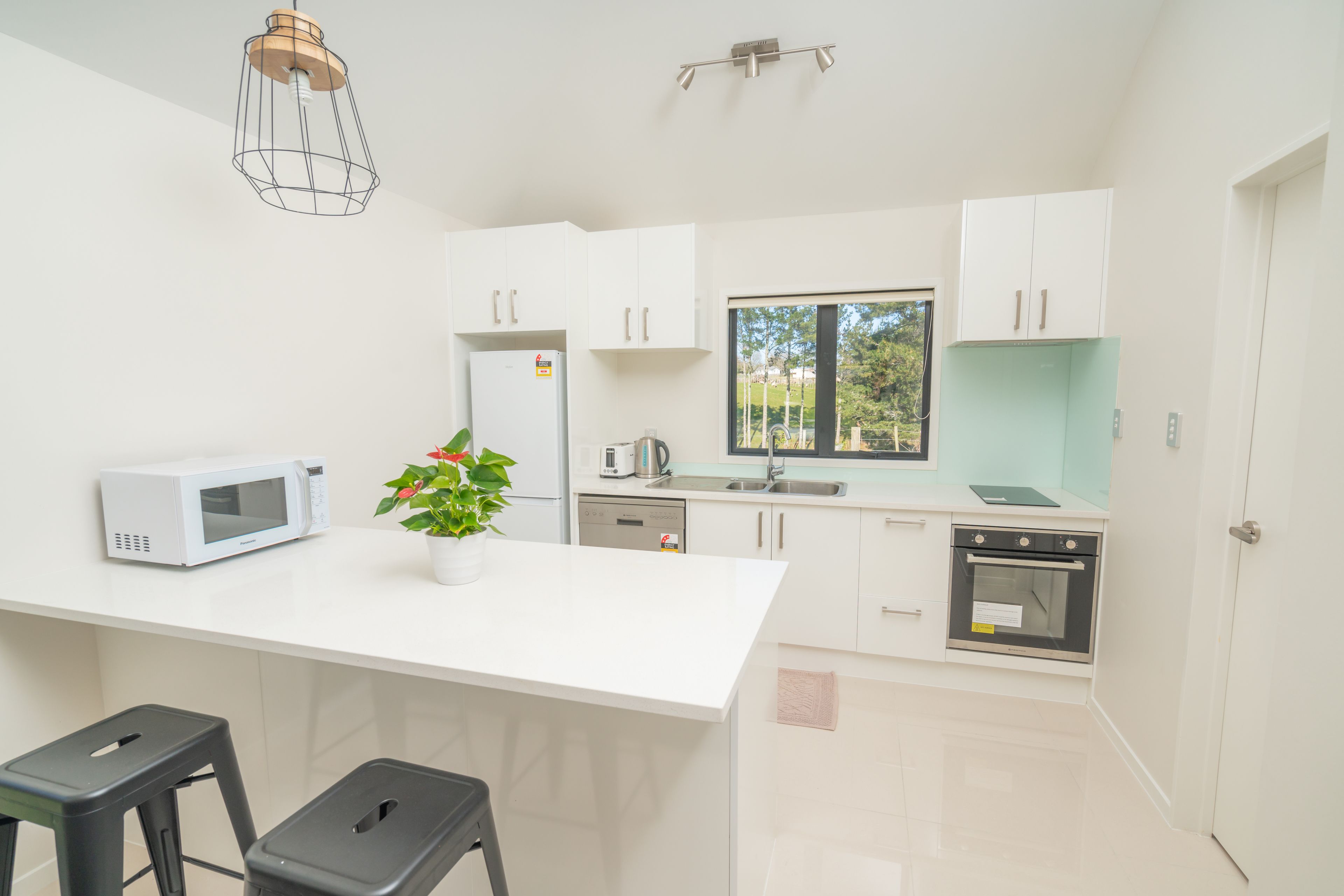 A modern kitchen with white cabinetry, a microwave, a coffee maker, and a potted plant.