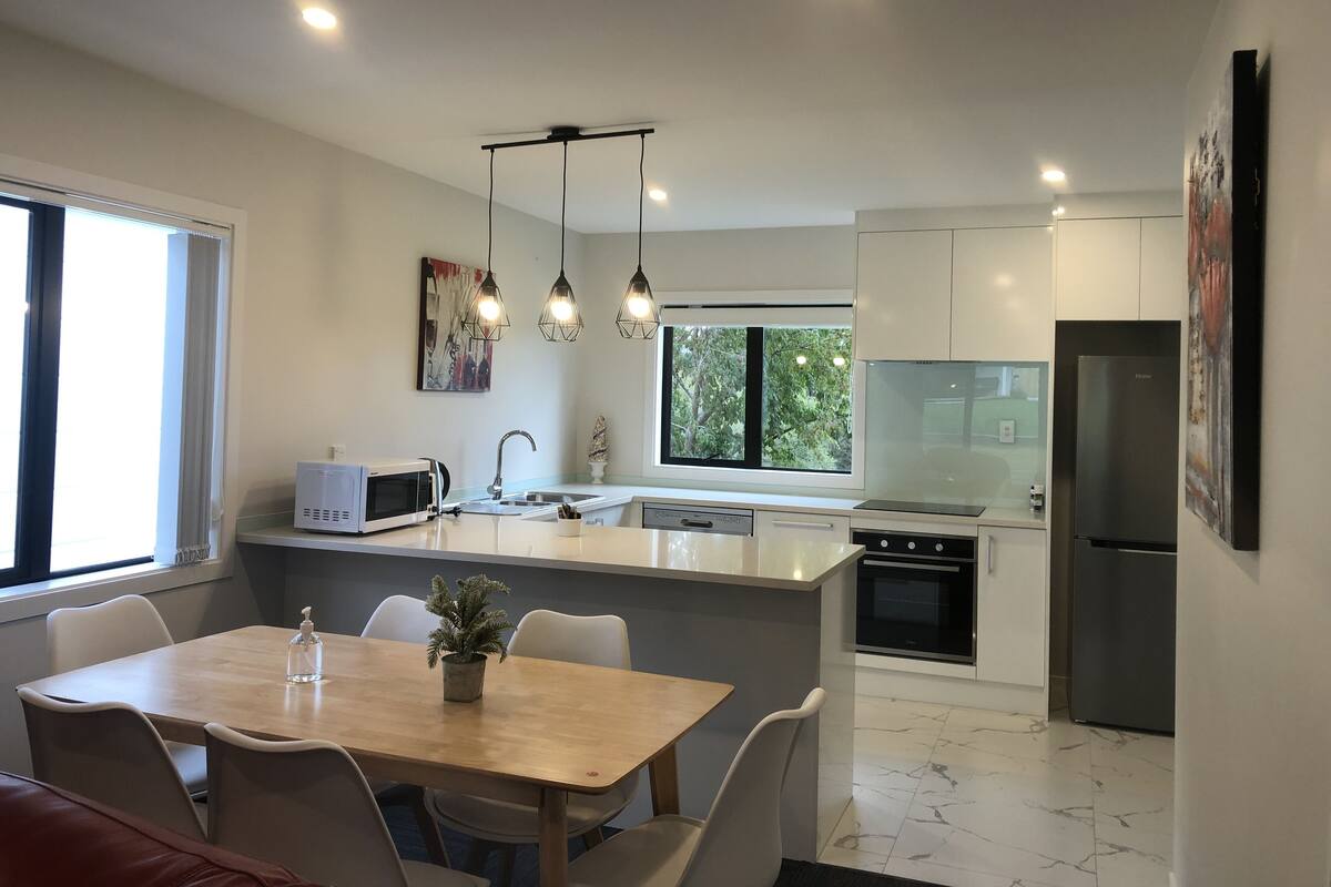 Una cucina moderna con isola centrale, zona pranzo con tavolo e sedie, e frigorifero.