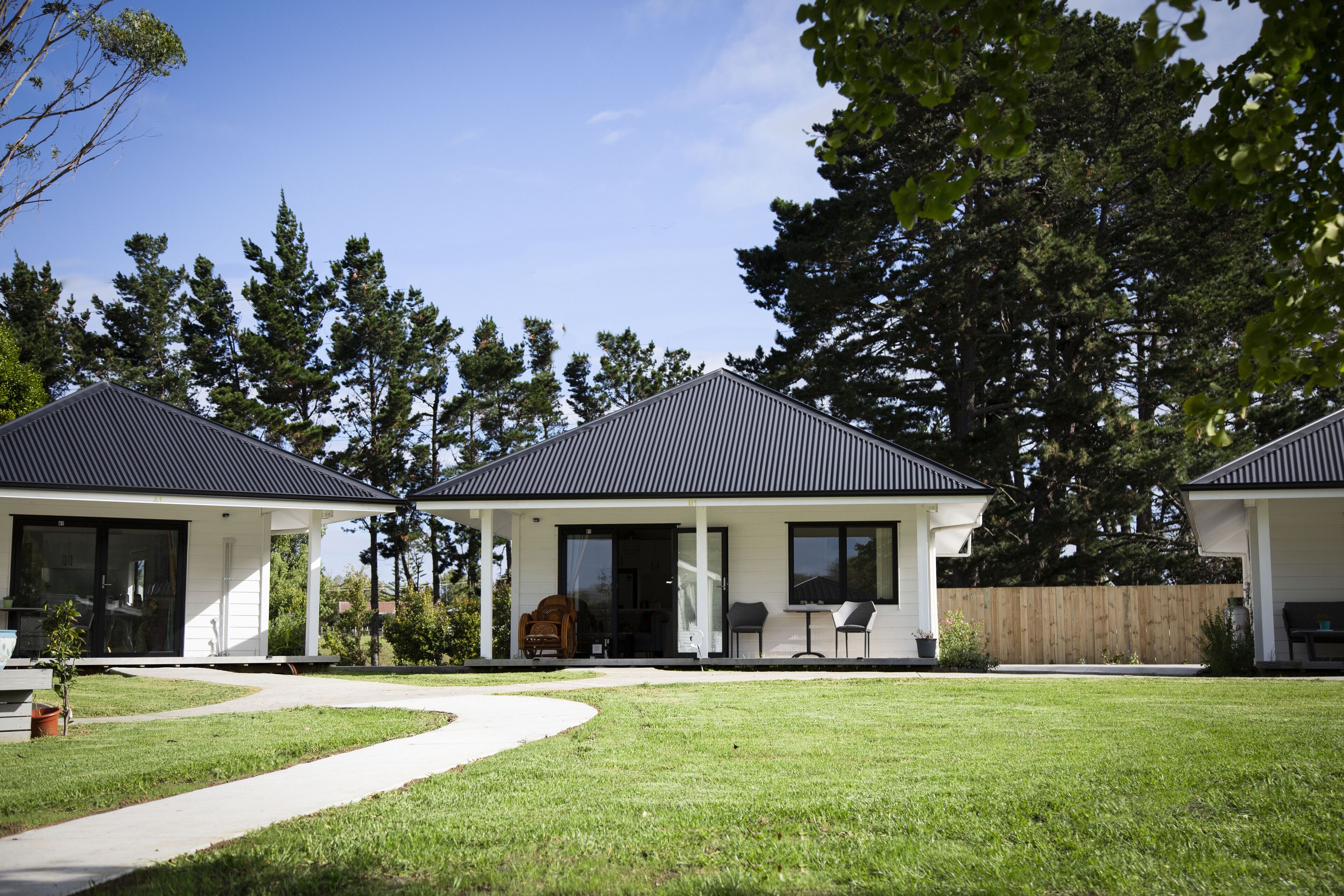 A modern two-story house with a covered patio, a lawn, and a wooden fence.