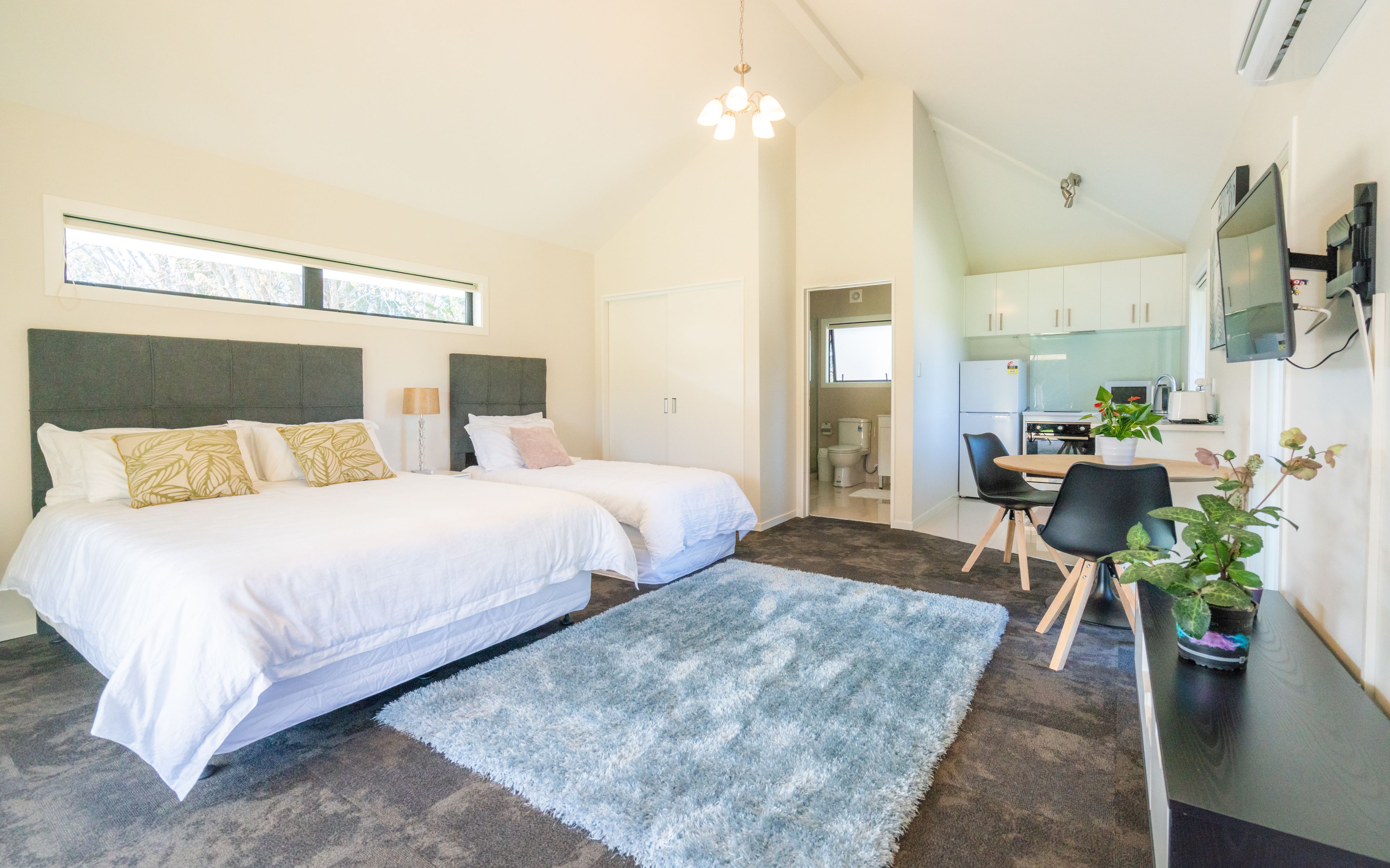 Quarto moderno com duas camas, uma escrivaninha e uma cozinha compacta.