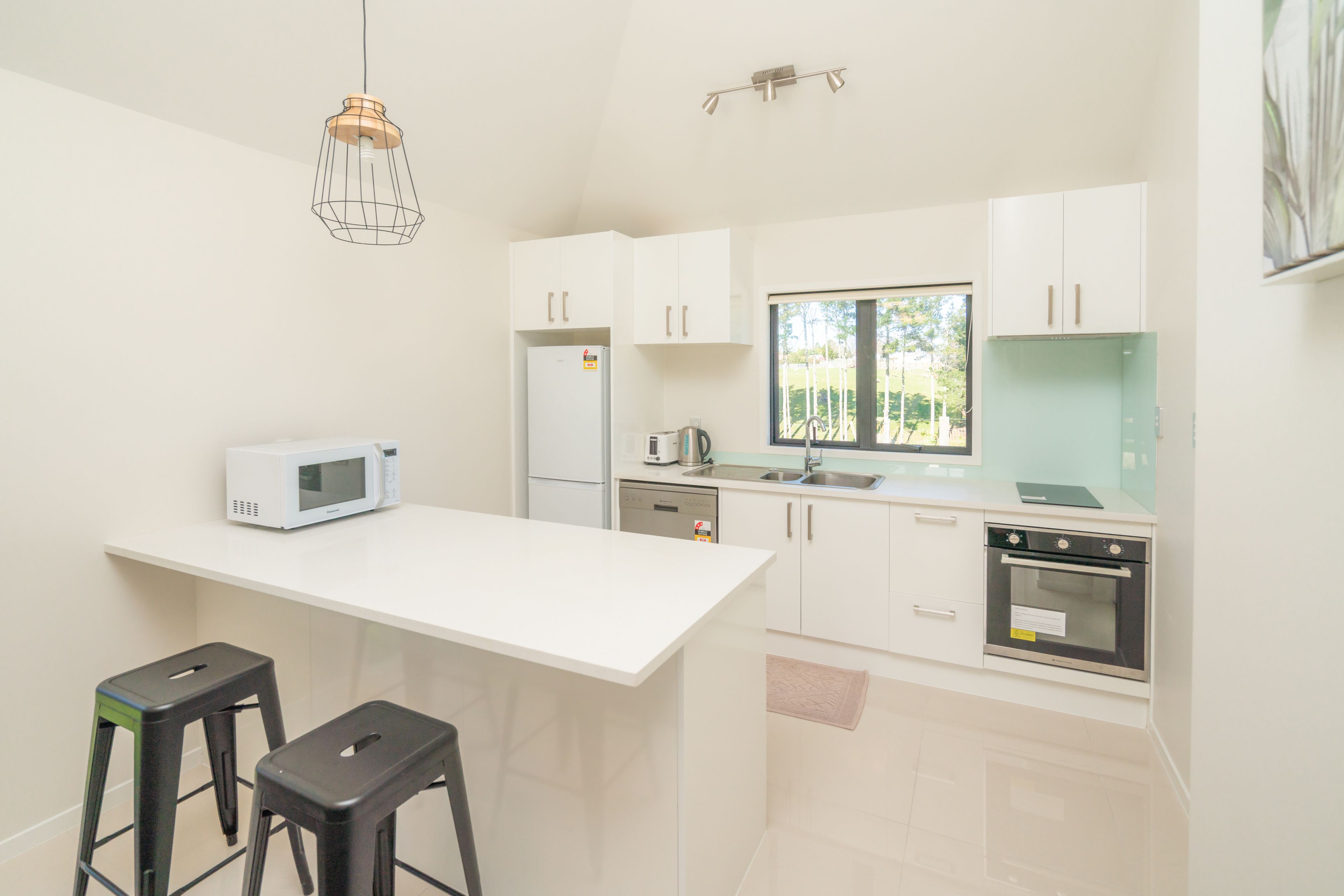 A modern kitchen with white cabinets, a microwave, a coffee maker, and a window.