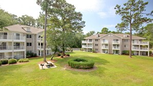 Um edifício residencial com vários andares, varandas, um gramado bem cuidado e árvores já crescidas.