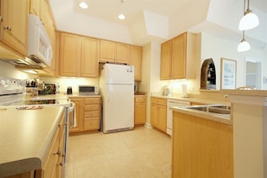 A modern kitchen with wooden cabinets, a built-in microwave, a refrigerator, and a dishwasher. - 708 Colony II (Sunset Beach)