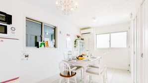Un comedor luminoso y blanco con una araña, un refrigerador y una ventana con vistas.