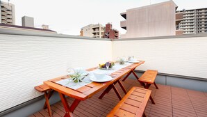 Terraza en la azotea con una mesa de madera dispuesta para comer, rodeada por un muro de ladrillo blanco.
