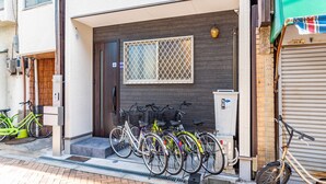Un edificio con una puerta de madera oscura y una ventana con celosía metálica. Hay bicicletas estacionadas frente al edificio.