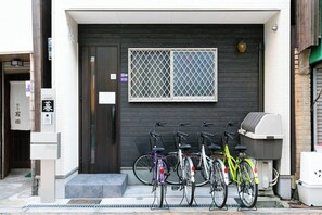 A building entrance with a dark door, a window with a grid pattern, and several bicycles parked outside. - Kashibesso Villa De Class (Osaka)
