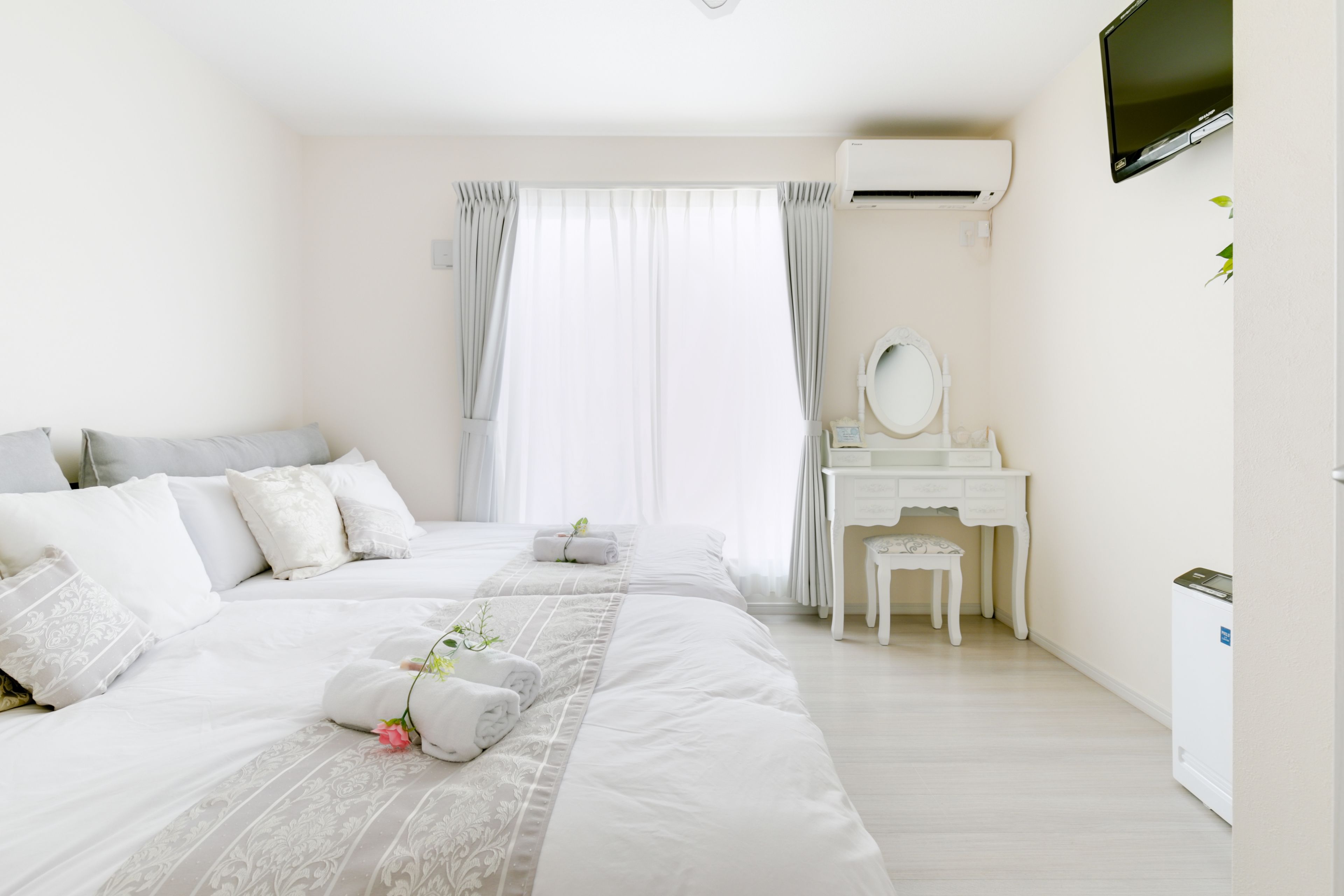 Habitación de hotel con dos camas, una tocador blanco, un televisor y un equipo de aire acondicionado blanco.