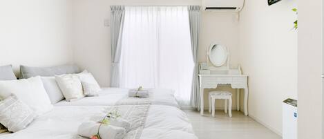 Habitación de hotel con dos camas, una tocador blanco, un televisor y un equipo de aire acondicionado blanco.