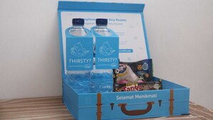 Una maleta azul con asa, que contiene dos botellas con la etiqueta "THIRSTY?" y una caja de bocadillos.