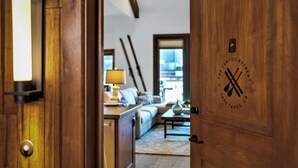 Eine Holztür mit einem Logo und Blick in ein Wohnzimmer mit Sofa, Couchtisch und Lampe.