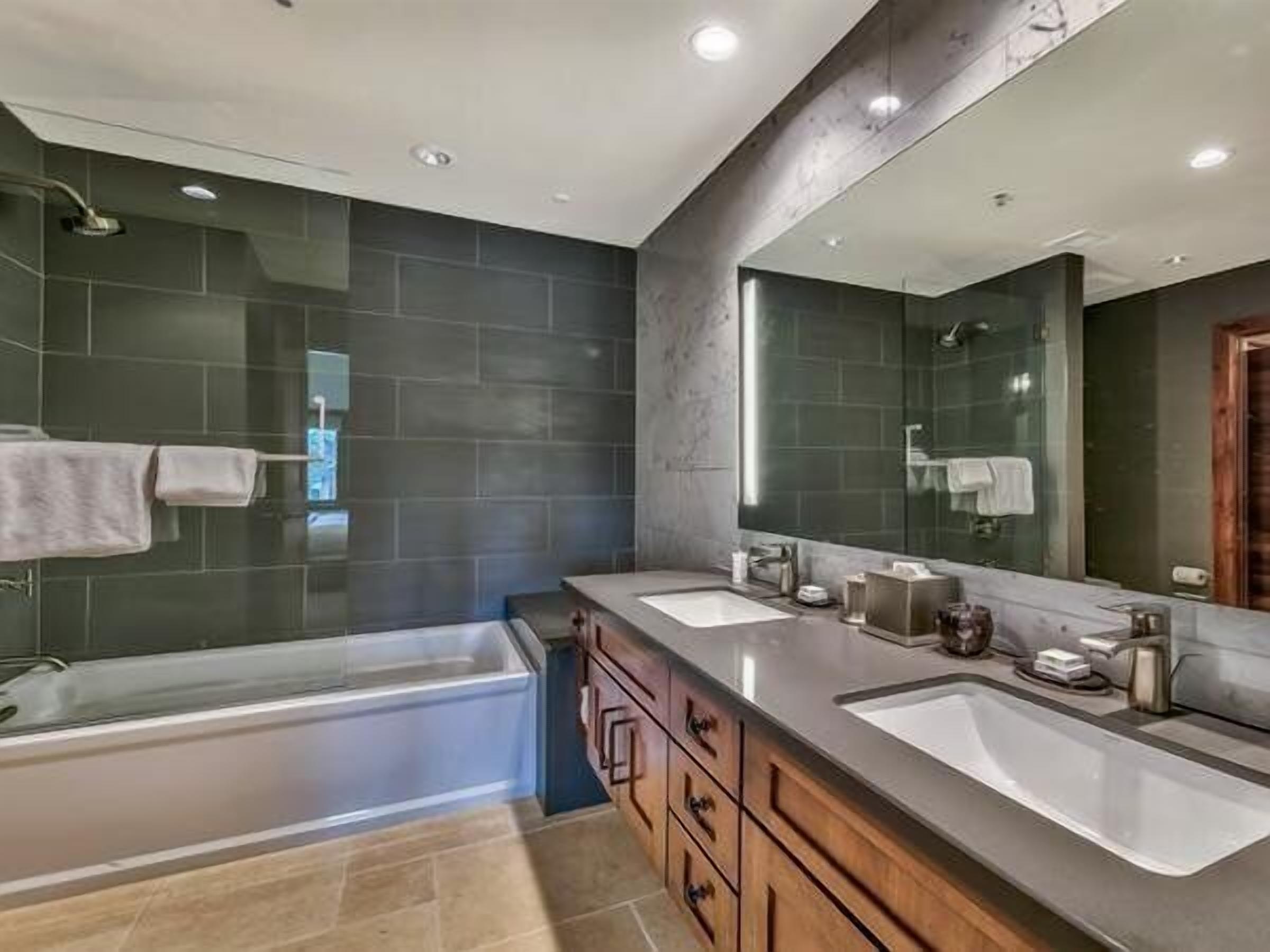 A modern bathroom with two sinks, a large mirror, and a bathtub.