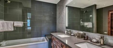 A modern bathroom with two sinks, a large mirror, and a bathtub.
